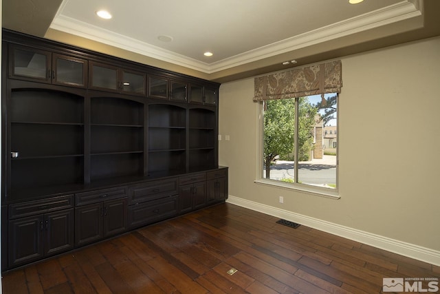 empty room with crown molding, dark wood finished floors, a raised ceiling, visible vents, and baseboards