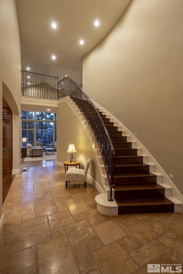 stairs with a high ceiling, baseboards, stone tile flooring, and recessed lighting