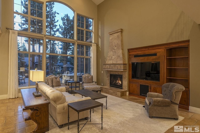 living room featuring stone tile floors, a fireplace, a towering ceiling, and baseboards