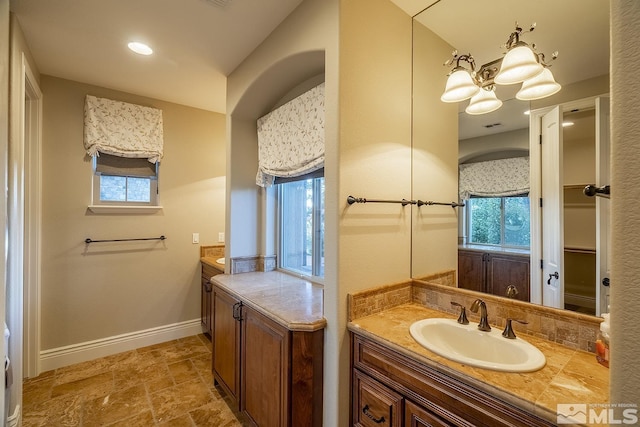 full bath featuring stone finish flooring, baseboards, a wealth of natural light, and vanity