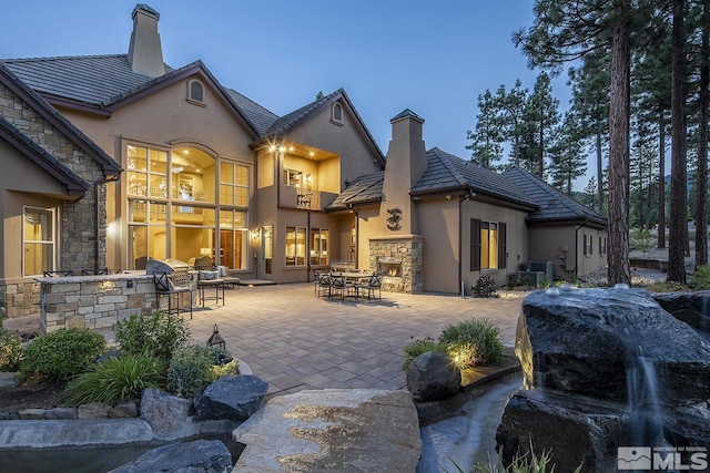 back of property featuring stone siding, a chimney, a patio area, and stucco siding