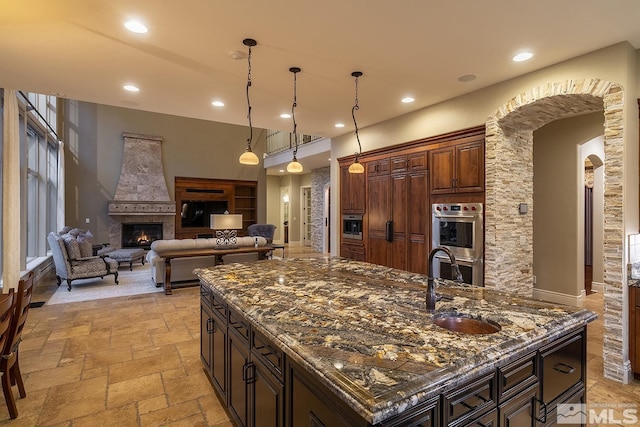 kitchen featuring stone tile floors, arched walkways, a glass covered fireplace, a spacious island, and double oven