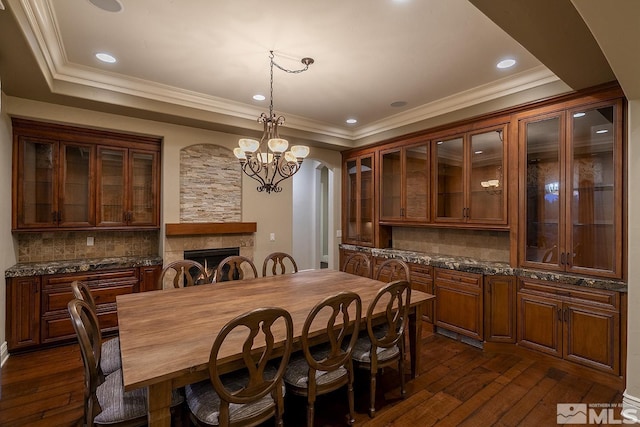 dining space with dark wood-style floors, arched walkways, a warm lit fireplace, and a tray ceiling