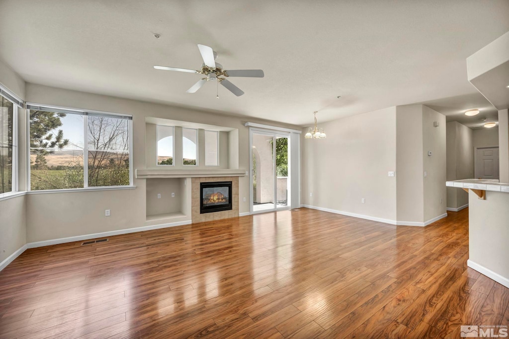 unfurnished living room with ceiling fan with notable chandelier, hardwood / wood-style floors, plenty of natural light, and a tiled fireplace