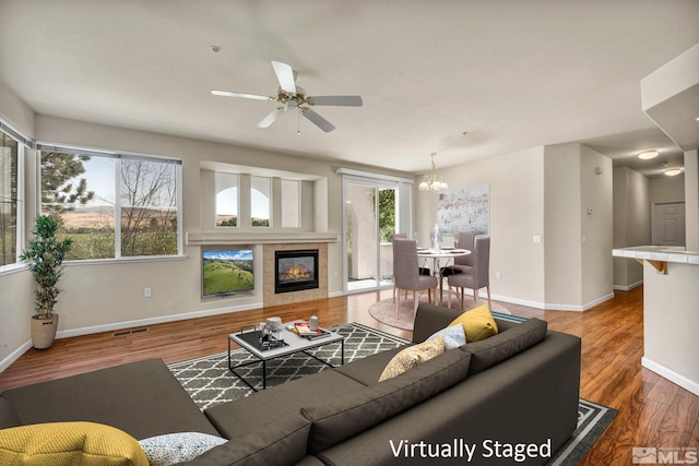 living room with ceiling fan with notable chandelier, hardwood / wood-style flooring, and a tiled fireplace