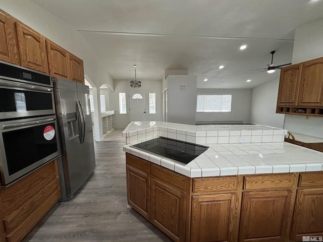 kitchen with a kitchen island, appliances with stainless steel finishes, wood finished floors, arched walkways, and a ceiling fan