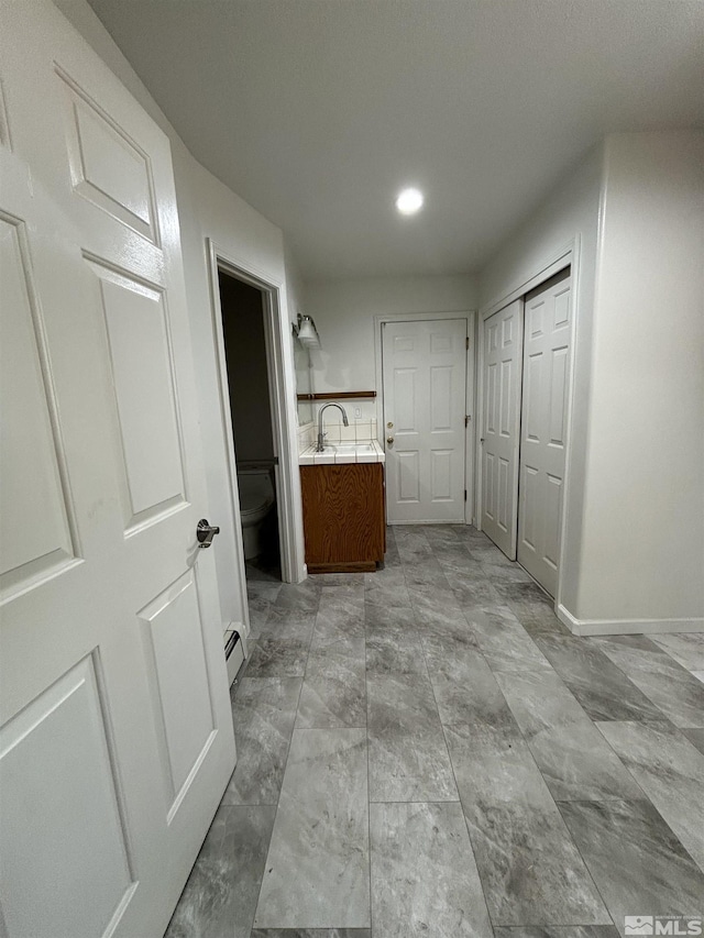 hall with recessed lighting, baseboards, baseboard heating, and a sink