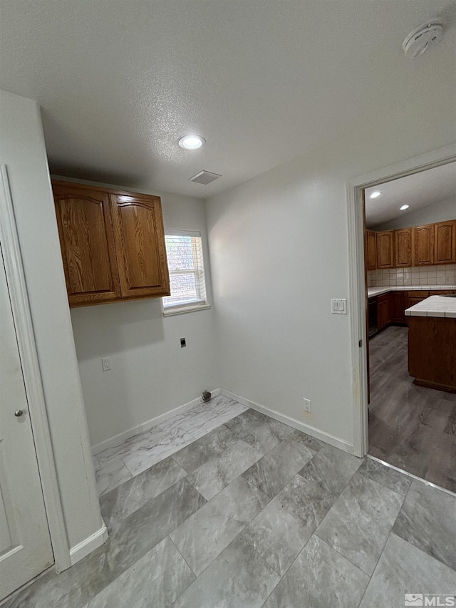 clothes washing area featuring electric dryer hookup, visible vents, a textured ceiling, cabinet space, and baseboards
