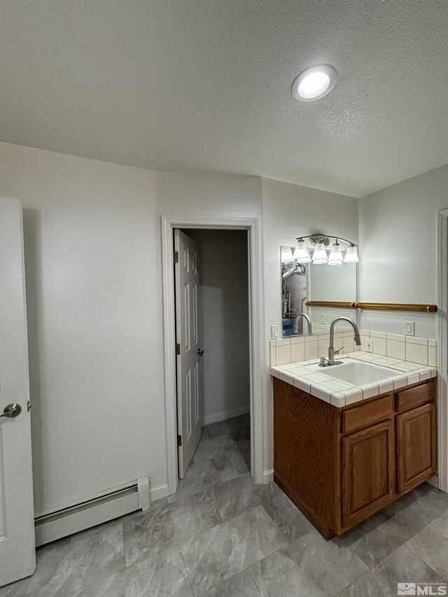 bathroom with a baseboard radiator, baseboards, a textured ceiling, and vanity
