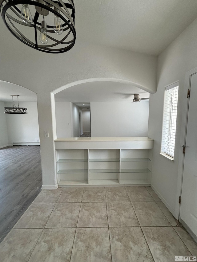 interior space featuring tile patterned floors, arched walkways, baseboards, and a chandelier