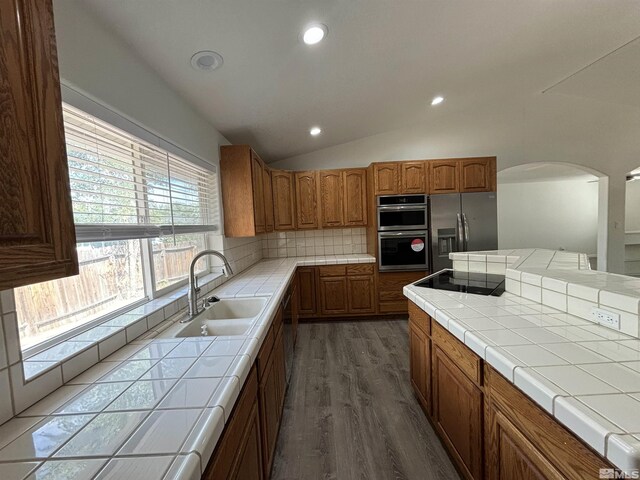 kitchen with vaulted ceiling, tile countertops, stainless steel appliances, sink, and dark wood-type flooring