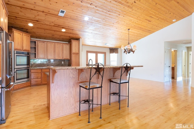 kitchen with a chandelier, appliances with stainless steel finishes, light wood-type flooring, and a kitchen bar