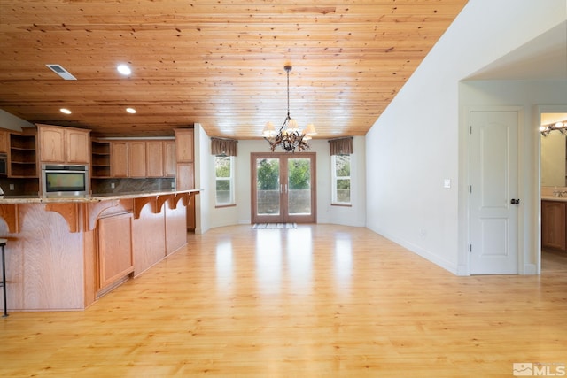 kitchen featuring a kitchen breakfast bar, light wood-type flooring, appliances with stainless steel finishes, decorative light fixtures, and a notable chandelier