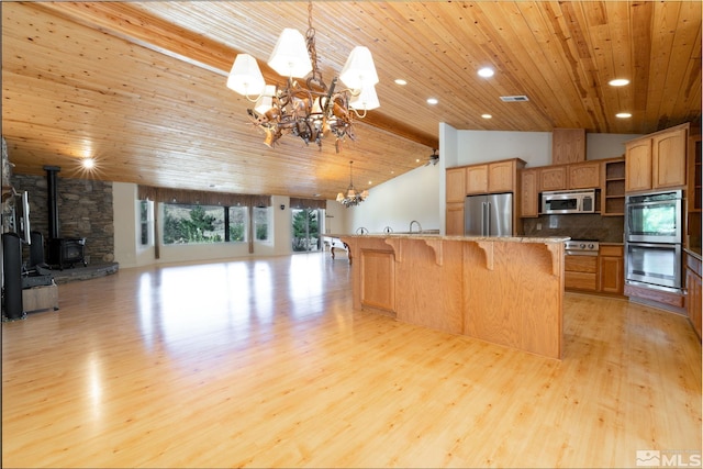 kitchen featuring wood ceiling, decorative light fixtures, a wood stove, and appliances with stainless steel finishes