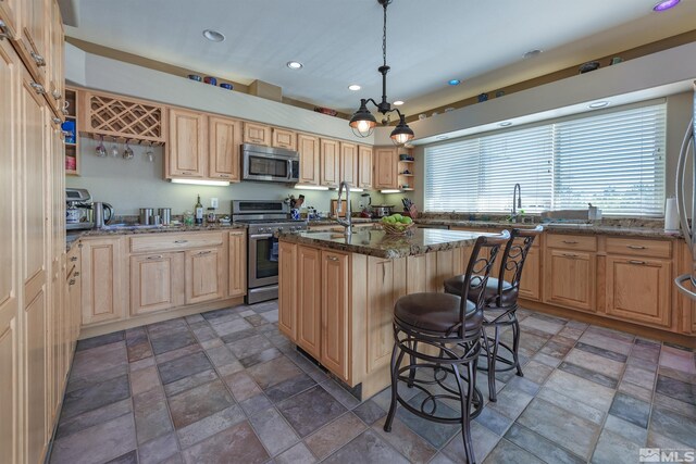 kitchen with appliances with stainless steel finishes, a chandelier, sink, an island with sink, and dark stone counters