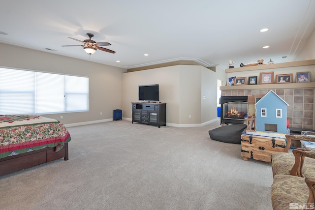 carpeted bedroom featuring ceiling fan, a tiled fireplace, and ornamental molding