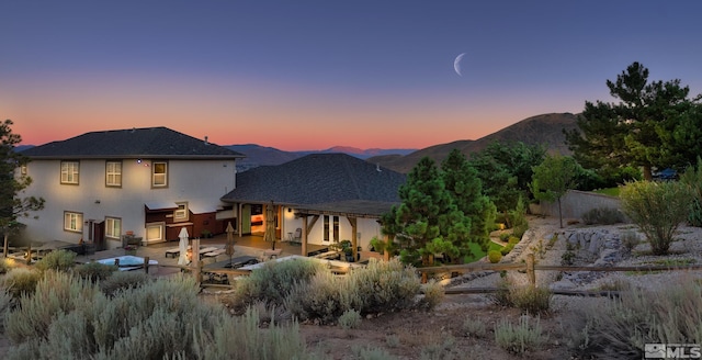 back house at dusk featuring a mountain view and a patio