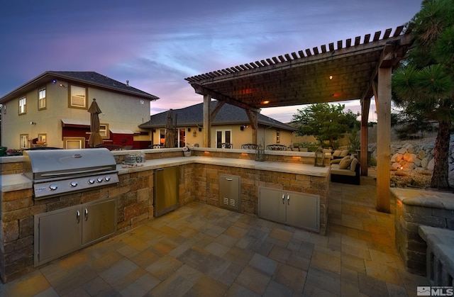 patio terrace at dusk with exterior kitchen, a pergola, and area for grilling