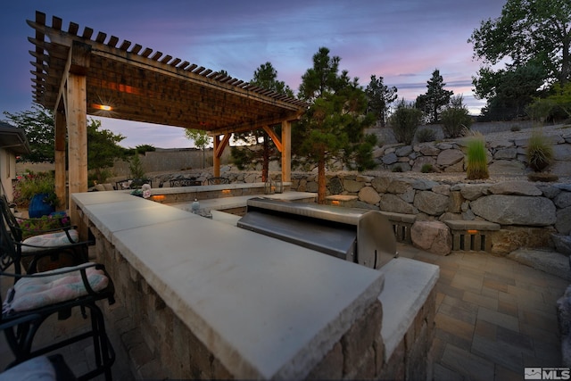 patio terrace at dusk featuring exterior bar and a pergola