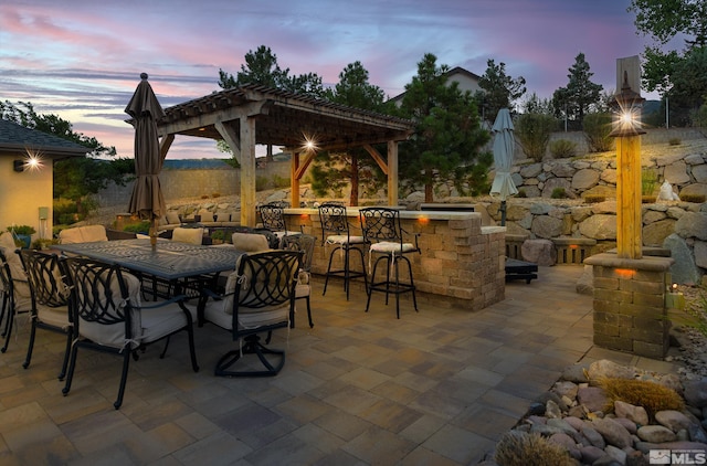 patio terrace at dusk featuring a pergola and exterior bar