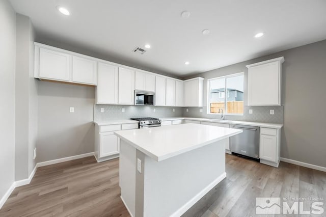 kitchen with white cabinets, light hardwood / wood-style floors, tasteful backsplash, a kitchen island, and stainless steel appliances