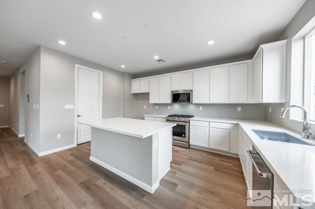 kitchen with white cabinets, sink, light hardwood / wood-style floors, appliances with stainless steel finishes, and a kitchen island