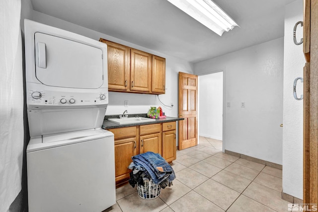 laundry area featuring light tile patterned flooring, cabinets, stacked washer and clothes dryer, and sink