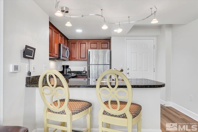 kitchen with appliances with stainless steel finishes, wood-type flooring, kitchen peninsula, and a kitchen breakfast bar