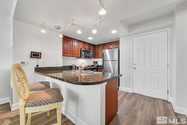 kitchen featuring stainless steel appliances, light hardwood / wood-style floors, kitchen peninsula, pendant lighting, and a breakfast bar