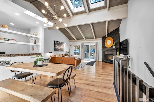 dining space featuring light hardwood / wood-style flooring, a notable chandelier, a large fireplace, high vaulted ceiling, and a skylight