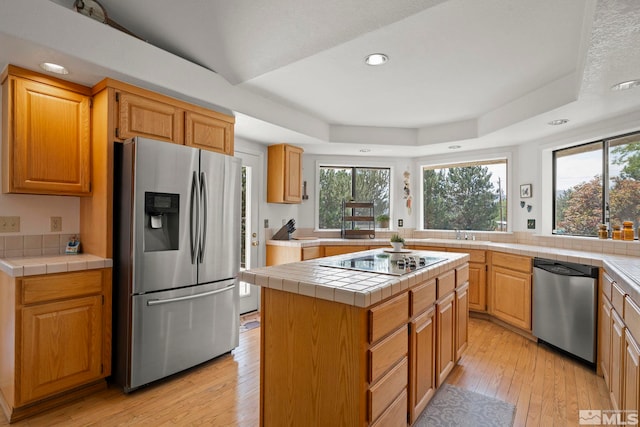 kitchen with tile counters, a center island, stainless steel appliances, and light wood-type flooring