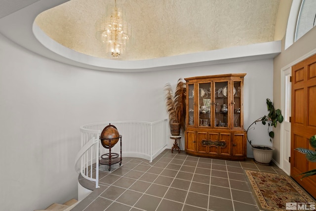 foyer with a towering ceiling, a raised ceiling, dark tile patterned flooring, and an inviting chandelier