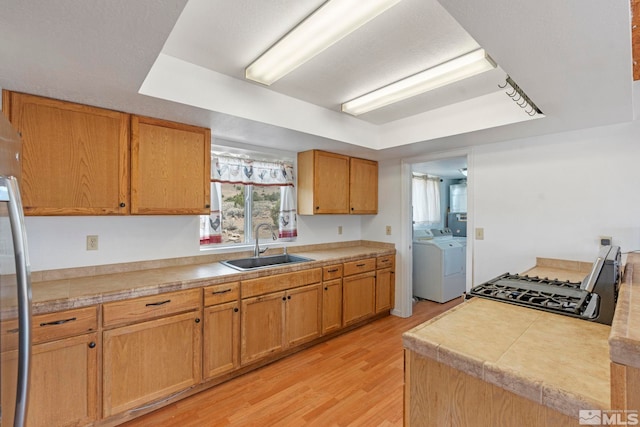 kitchen with stainless steel range oven, washer and clothes dryer, sink, and light wood-type flooring