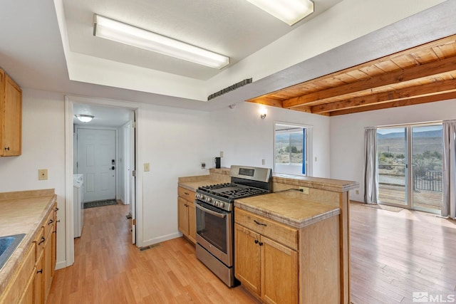 kitchen featuring stainless steel range with gas stovetop, washer / clothes dryer, light wood-type flooring, and beam ceiling