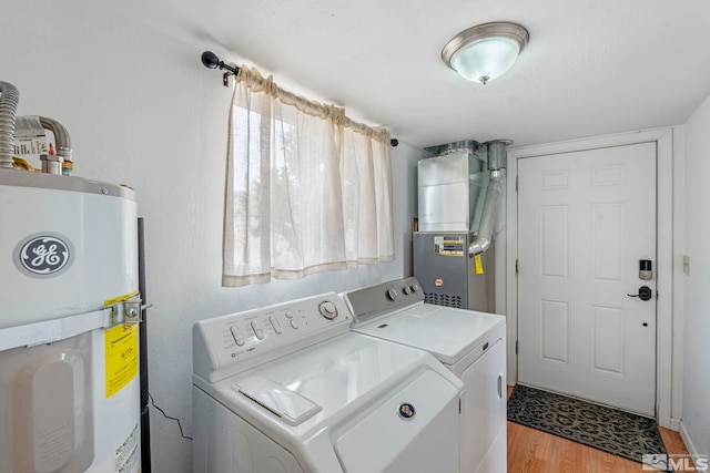 washroom with light hardwood / wood-style flooring, separate washer and dryer, electric water heater, and heating unit