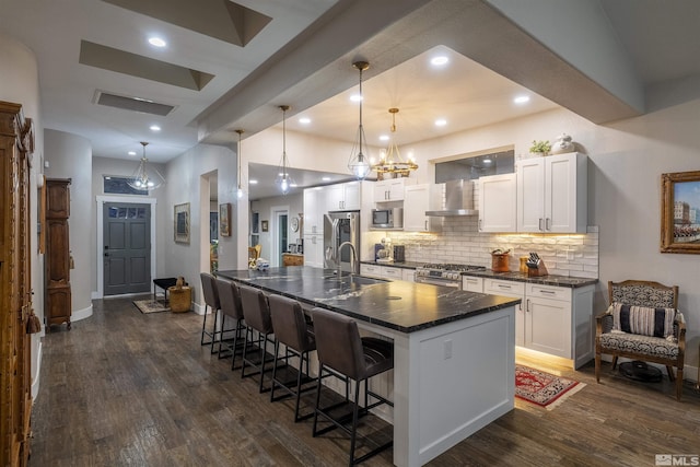 kitchen with a breakfast bar, dark wood-style flooring, stainless steel appliances, dark countertops, and wall chimney range hood