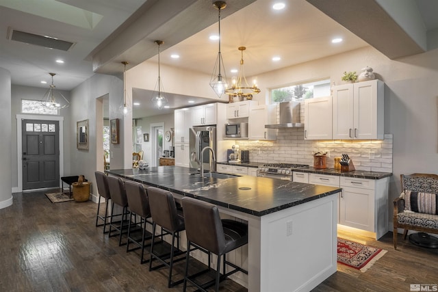 kitchen with dark wood finished floors, a sink, appliances with stainless steel finishes, dark countertops, and wall chimney exhaust hood