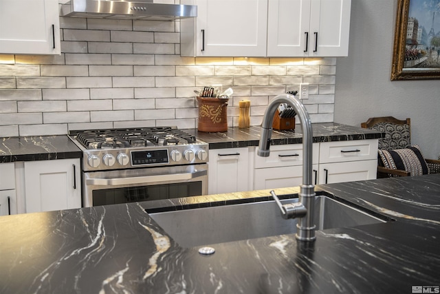 kitchen with under cabinet range hood, gas range, backsplash, and white cabinetry