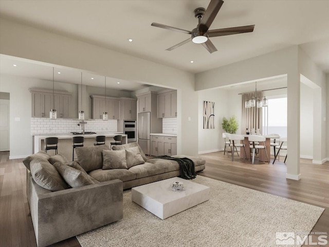 living room with ceiling fan with notable chandelier, wood-type flooring, and sink