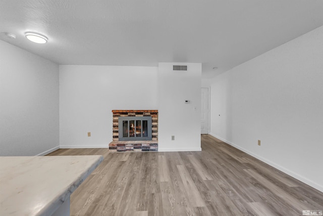 unfurnished living room featuring visible vents, wood finished floors, baseboards, and a glass covered fireplace