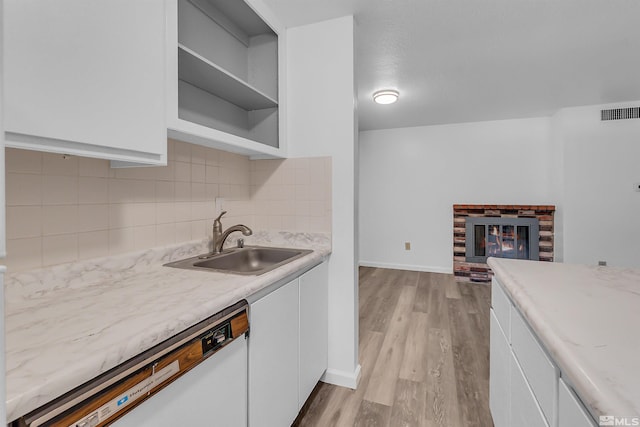 kitchen featuring a brick fireplace, decorative backsplash, white dishwasher, white cabinetry, and a sink