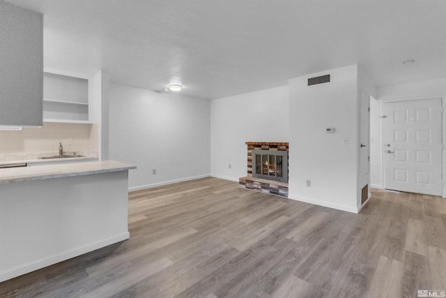 unfurnished living room with a glass covered fireplace, light wood-style flooring, visible vents, and a sink