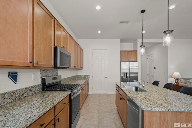 kitchen with visible vents, a sink, light stone countertops, appliances with stainless steel finishes, and a kitchen island with sink