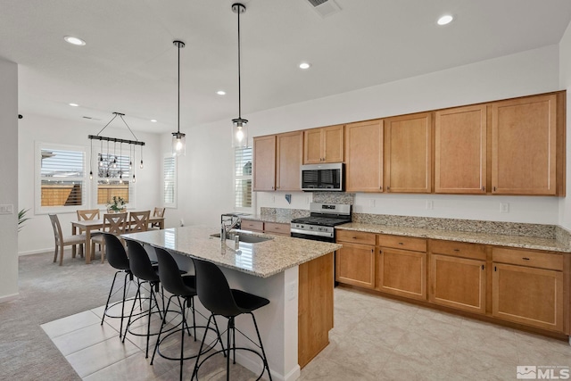 kitchen with visible vents, an island with sink, light stone counters, stainless steel appliances, and a sink