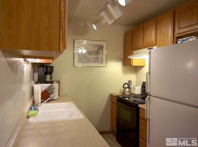 kitchen with black electric range oven, sink, and white refrigerator