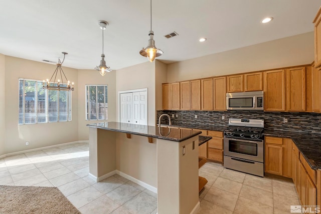 kitchen featuring a center island with sink, dark stone countertops, appliances with stainless steel finishes, and a chandelier