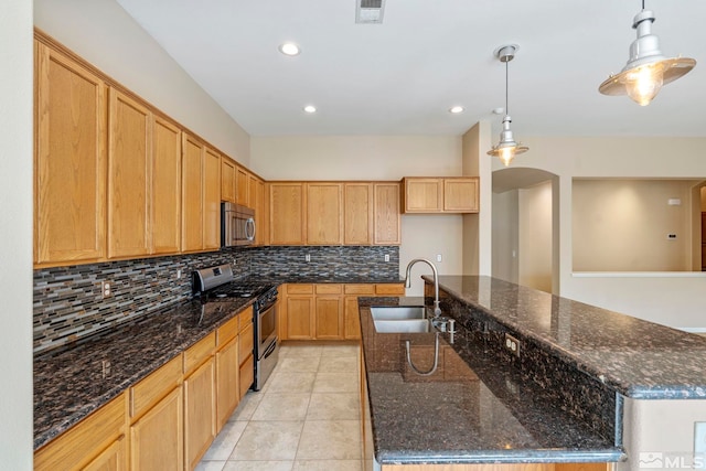 kitchen with an island with sink, pendant lighting, stainless steel appliances, and dark stone countertops