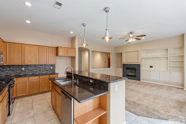 kitchen with a tile fireplace, appliances with stainless steel finishes, an island with sink, sink, and ceiling fan