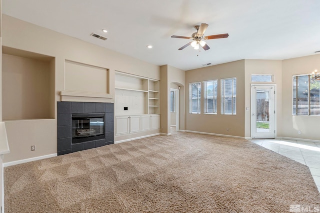 unfurnished living room with built in features, light colored carpet, ceiling fan with notable chandelier, and a fireplace