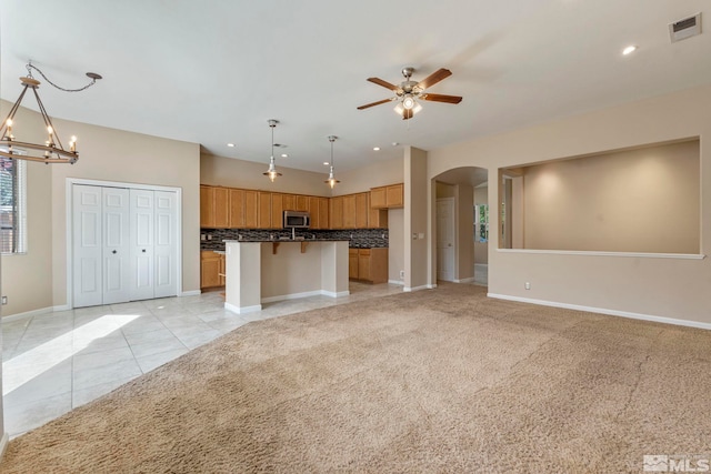 interior space with light tile patterned floors, a center island, decorative light fixtures, ceiling fan with notable chandelier, and a kitchen breakfast bar